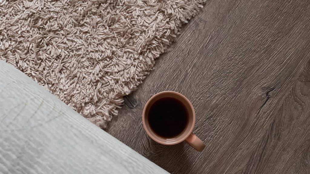 Ein Holzfußboden mit einem Teppich und einer Tasse Kaffee, der eine warme und einladende Atmosphäre schafft.